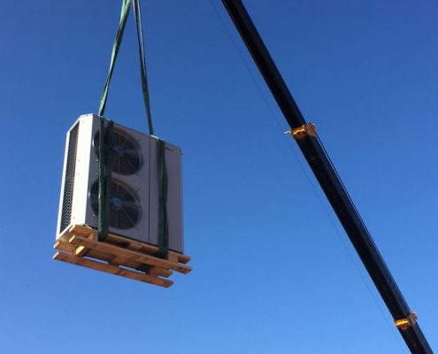 An outdoor condensing unit being craned onto a roof